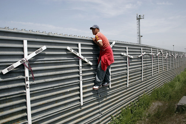 An aspiring migrant from Mexico crosses into the US at the Tijuana-San Diego border. The crosses on the fence represent the deaths of failed attempts.