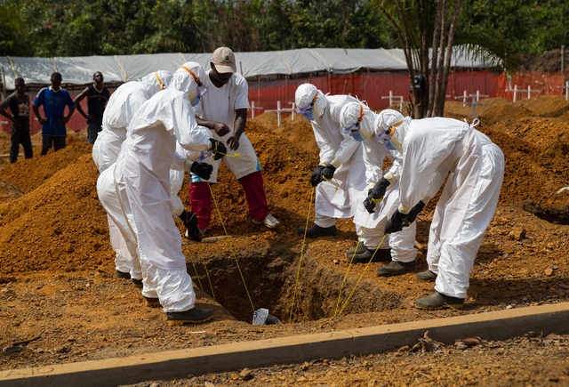 Health workers in West Africa lower an ebola victim into the ground in a safe burial process