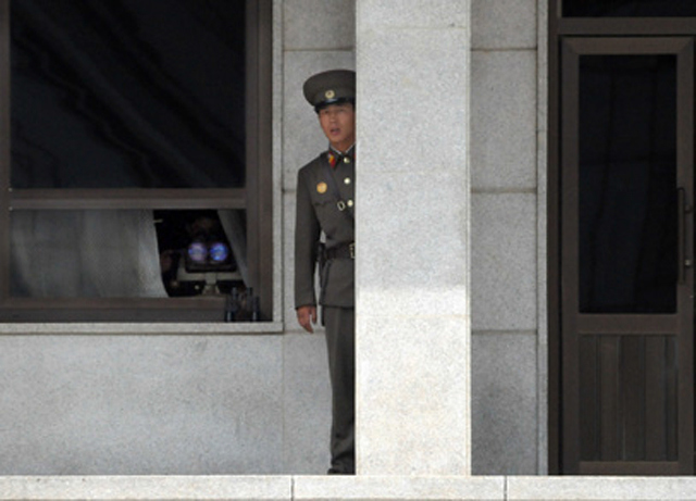 DPRK Guard peers out from behind a granite pillar.